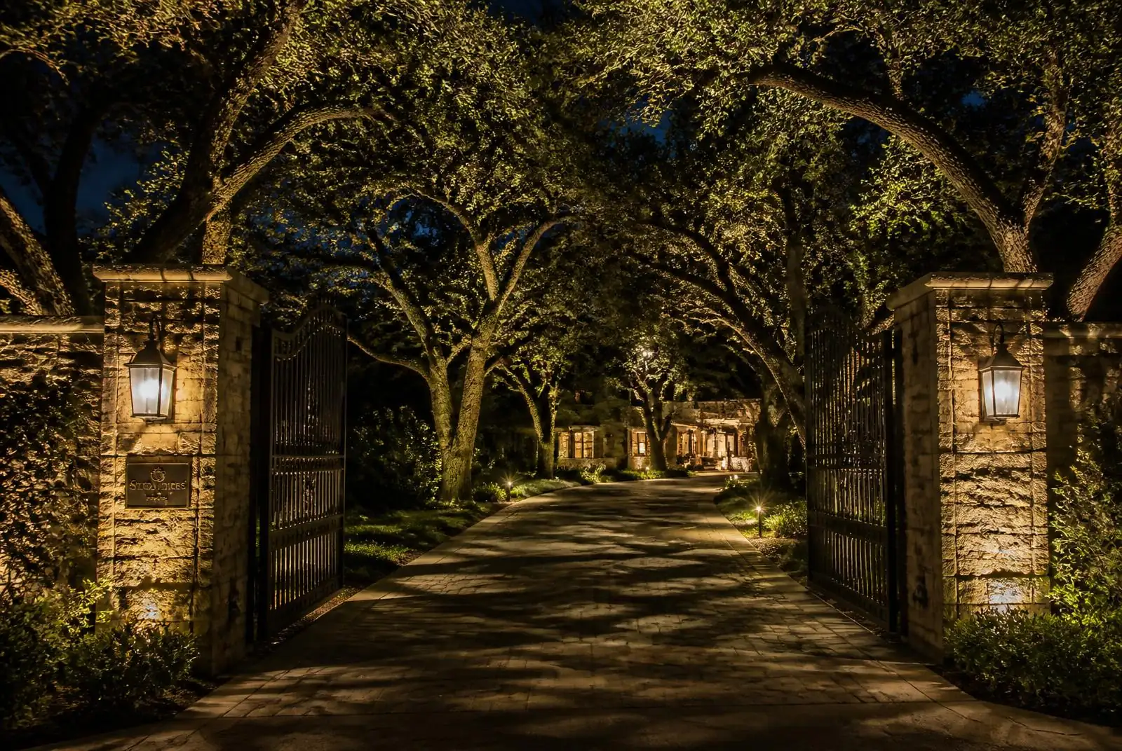 San Juan Capistrano gated estate driveway with lit oaks and stone pilasters at night
